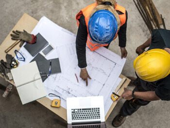 Team members wearing safety gear discussing blue prints 